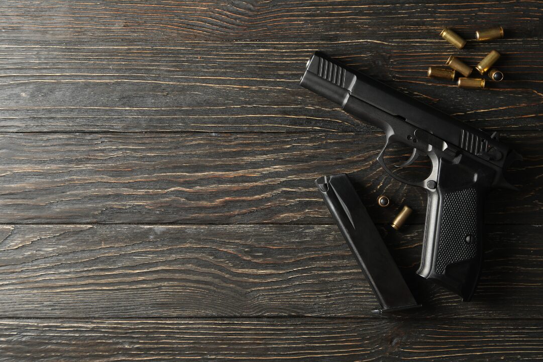 Pistol with bullets and magazine on wooden background for ammo and reloading themes.