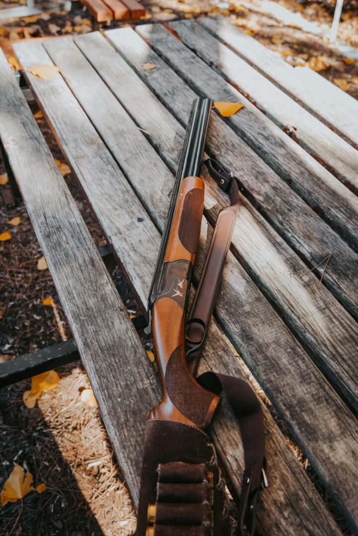 Hunting shotgun on rustic wooden bench outdoors for hunting and outdoor firearm visuals.
